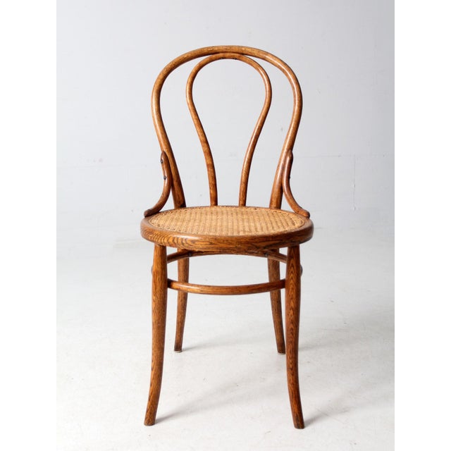 This vintage bentwood chair captures the elegance of Thonet-inspired design with its gracefully curved backrest, woven...