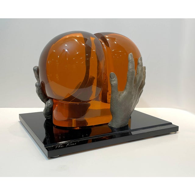 Bernard Pfreim, "The Kiss", Amber Acrylic Sculpture, having silvered resin hands, resting on a black acrylic base.