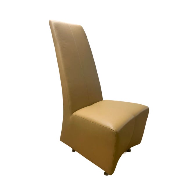 The Elika chair by Brueton, in tan leather, is a sleek, tall and slender dining chair. It measures 49.5"H x 20"W x 24"D...