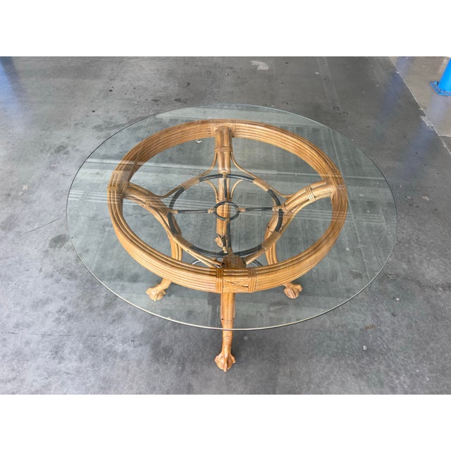 A vintage Palm Beach Regency style rattan dining table featuring a sculptural pencil reed base and thick round glass top....