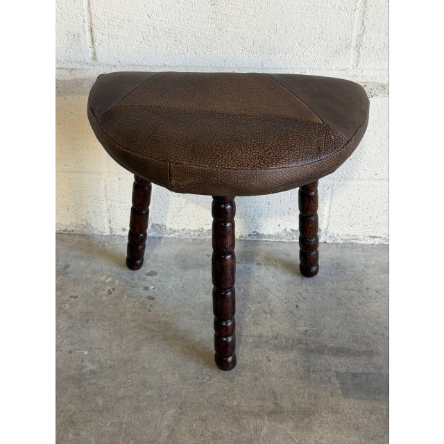 A three legs stool featuring a cushioned top paired with turned wooden support posts. Its organic tripod silhouette brings...