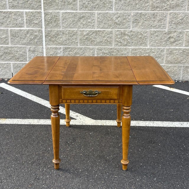 A late 20th century Ethan Allen Heirloom collection Traditional solid maple side table having a beveled drop leaf top over...
