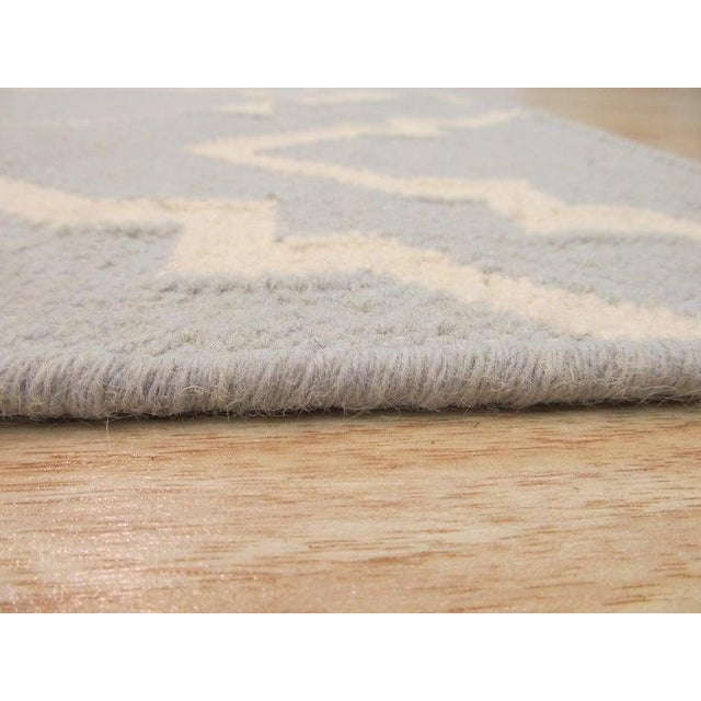 This gray wool rug is a flat weave floor covering designed in the traditional Dhurrie style. It serves as a functional...