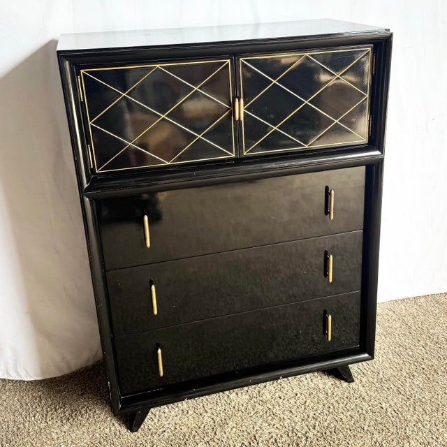 This Art Deco highboy dresser embodies glamour and function with its glossy black lacquered finish and refined gold...