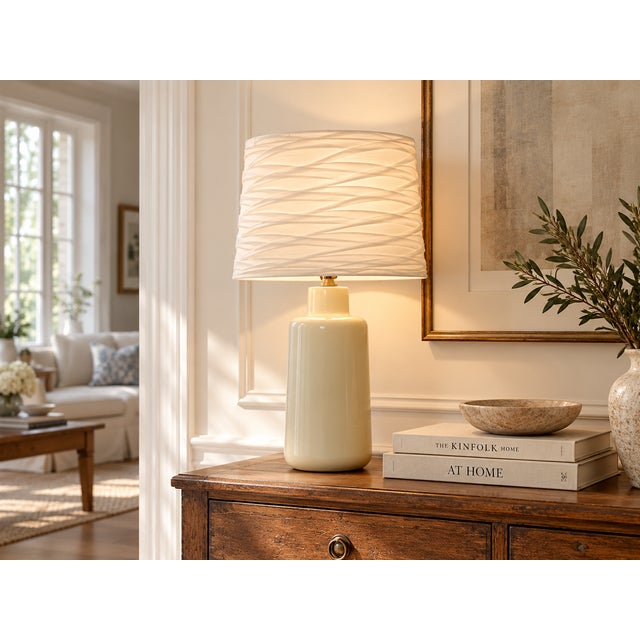 A tall, clean-lined pottery lamp in a soft buttercream glaze, the creamy yellow of fresh butter that looks warmer in...