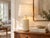 A tall, clean-lined pottery lamp in a soft buttercream glaze, the creamy yellow of fresh butter that looks warmer in...