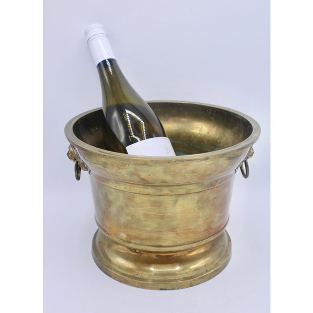 A charming vintage English Brass champagne ice bucket or planter with lion's head ring handles, circa 1950s. The base is...