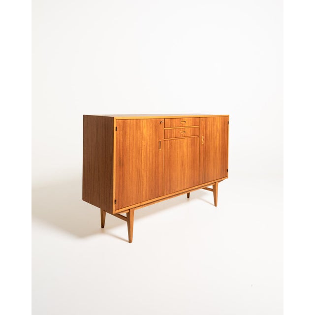 Teak highboard with oak trim, three hinged doors, and two central drawers with shaped handles. Scandinavian production,...