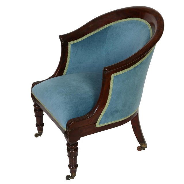 An English Regency style mahogany library chair featuring a tub form silhouette with a gently curved, wraparound back and...