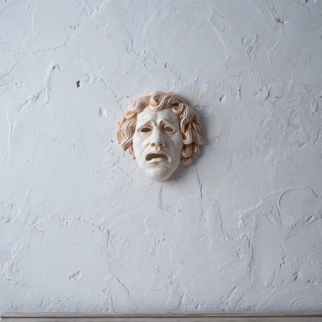 Cast plaster tragedy mask of classical male with anguished open-mouthed grimace, furrowed brows, and radiating curls, warm...