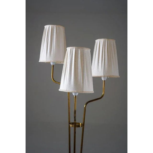 A graceful Swedish floor lamp from the 1940s, featuring a brass construction with three elegantly curved arms rising from...