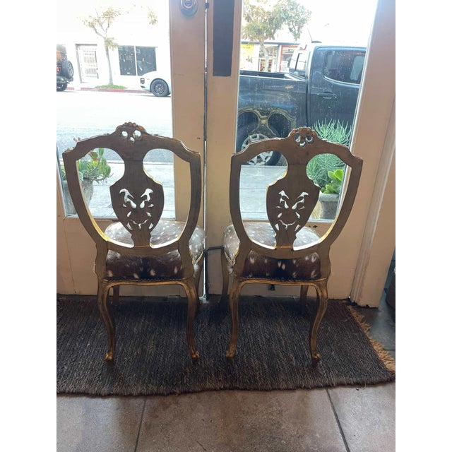 A striking pair of gilded antique Louis chairs, newly reupholstered in genuine deer hide. These chairs feature beautifully...