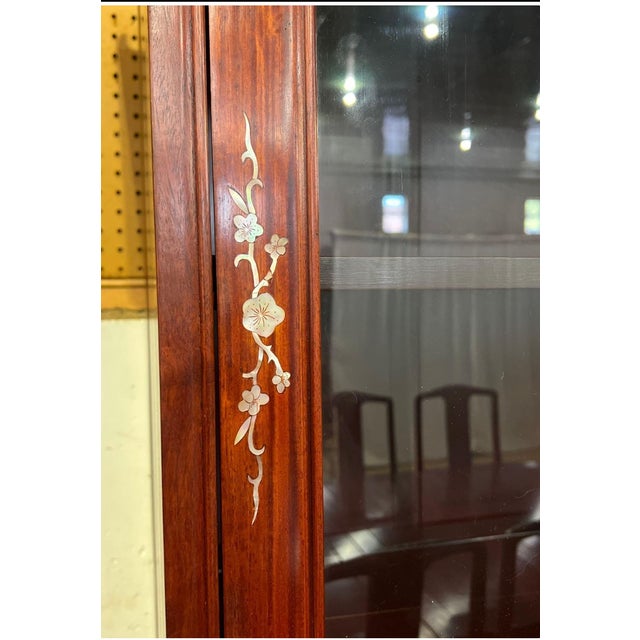 Two-piece solid rosewood china cabinet with mother-of-pearl plum blossom inlay and upturned cornice ends. Upper section...