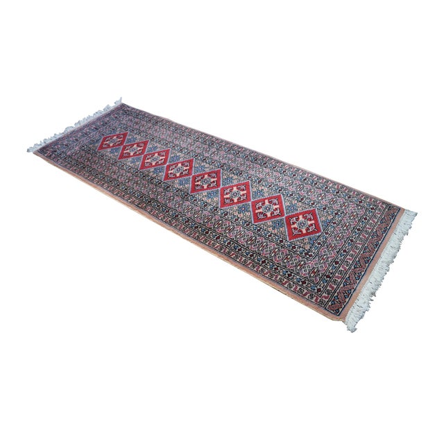 Vintage Pakistan 100% wool Oriental rug runner featuring a geometric diamond pattern in reds, pink, beige, and blues....