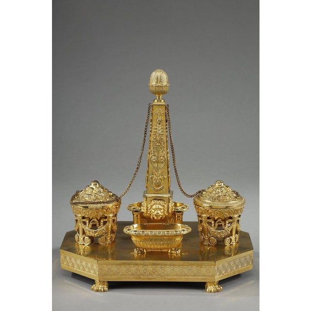 Chased and gilded bronze inkwell on a canted base with a frieze of interlacings centered on rosettes. Leobelisk model,...