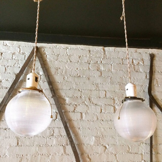 Pair of Industrial, Holophane glass, globe pendant lights feature porcelain sockets with pull chains and brass fitters are...