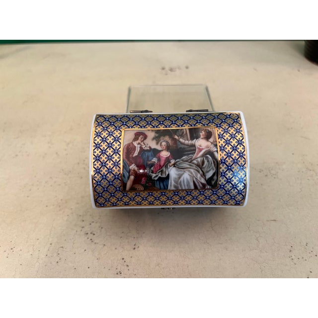 Beautiful porcelain trinket box painted on four sides in a blue and gold pattern. The top is adorned with a victorian...