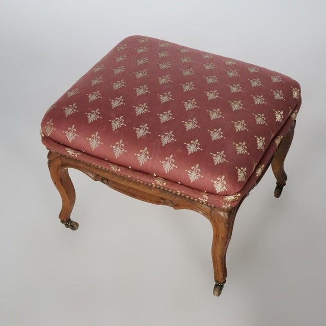 An antique French style footstool offers upholstered seat over walnut base having carved skirt and cabriole legs, C1920....