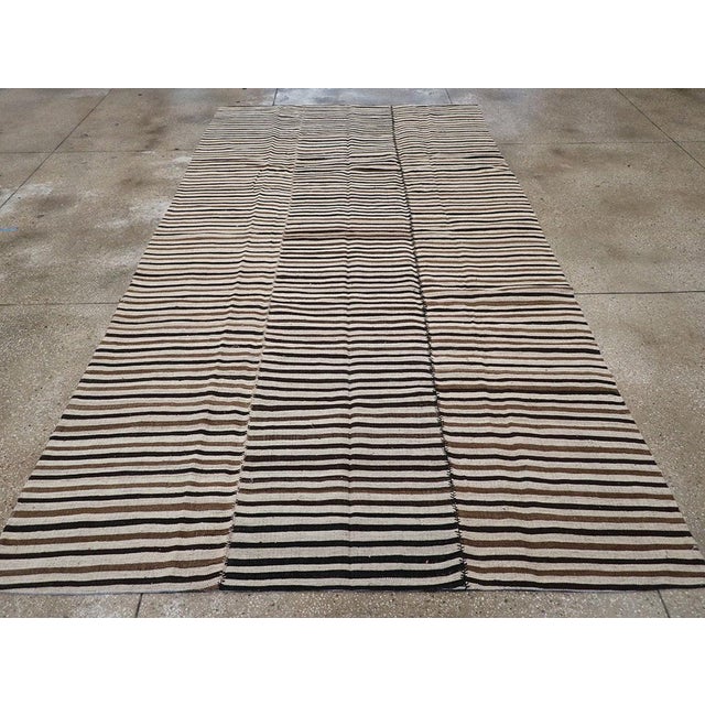 This mid-20th century Persian flatweave kilim rug, measuring 6' 10" x 12' 10", features a beautifully balanced striped...