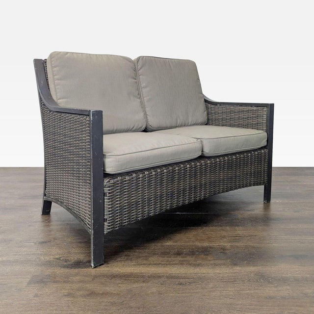 This outdoor loveseat features a sturdy dark frame with a woven all weather wicker design and thick, comfy gray cushions....