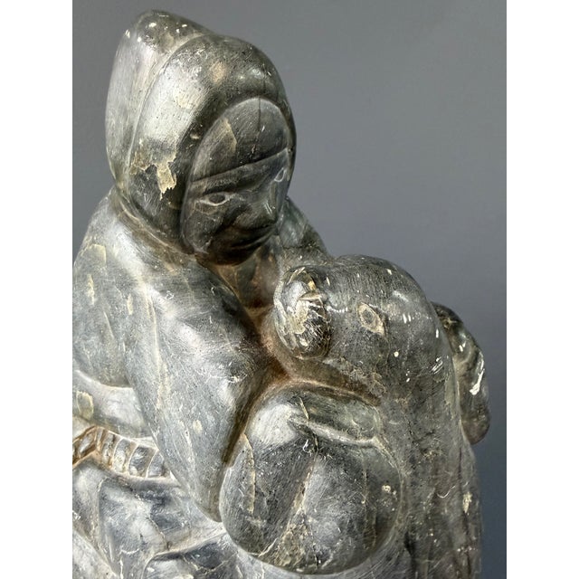 A compelling Inuit soapstone sculpture depicting a bundled hunter holding a seal, a subject deeply rooted in Arctic life...