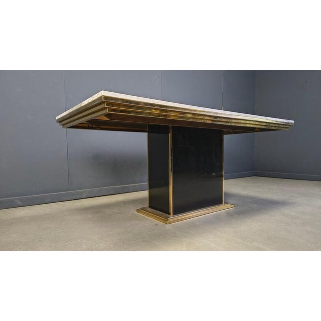 Large dining table with a white marble top, a brass frame and a brass and black glass base. The combination of these...