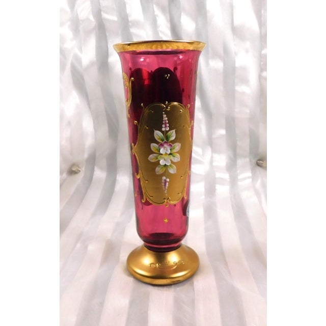 This is a pink glass footed vase that has dimensional flowers and gold trim. The base is painted gold with a raised design...