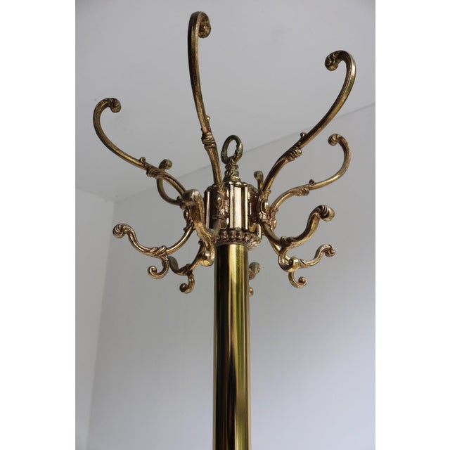 This ornate metal standing coat rack with a gold patina dates to the 1960s, a true vintage piece that blends functionality...