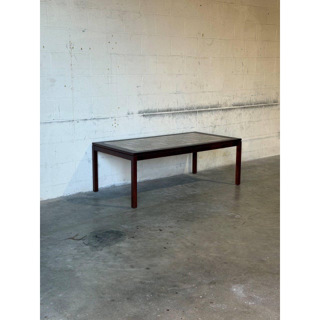This rectangular coffee table features a minimalist profile elevated by straight legs. The expansive top is inset with...