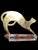 A brass cat sculpture on a clear acrylic base stylized with a smooth, elongated body and a tail curled under. The cat is...