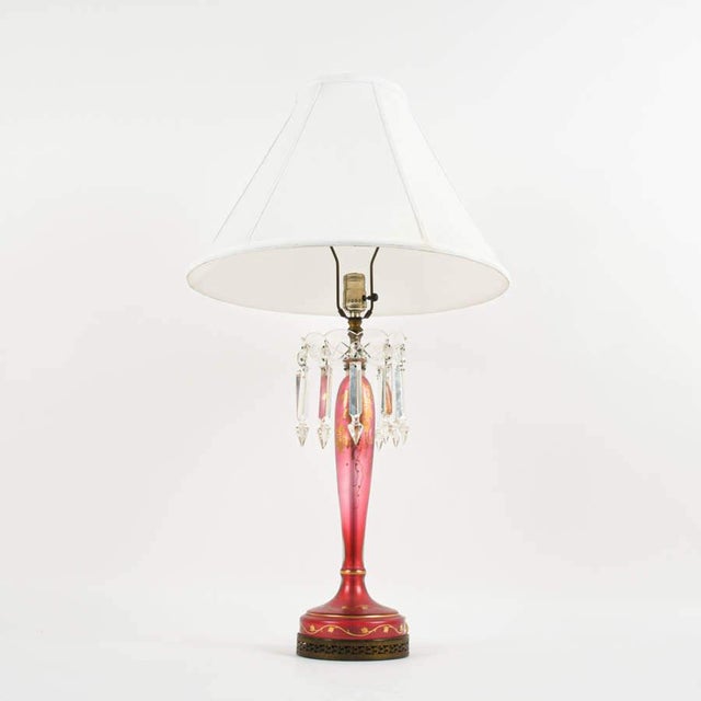 This decorative table lamp features a striking ruby red glass stem with elegant tapering form, accented by applied gilt...