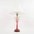 This decorative table lamp features a striking ruby red glass stem with elegant tapering form, accented by applied gilt...