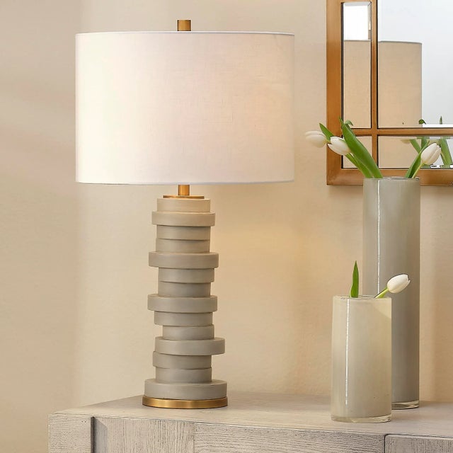 Discs of cement colored resin are stacked, seemingly haphazardly, in this whimsical lamp inspired by cairns, the...