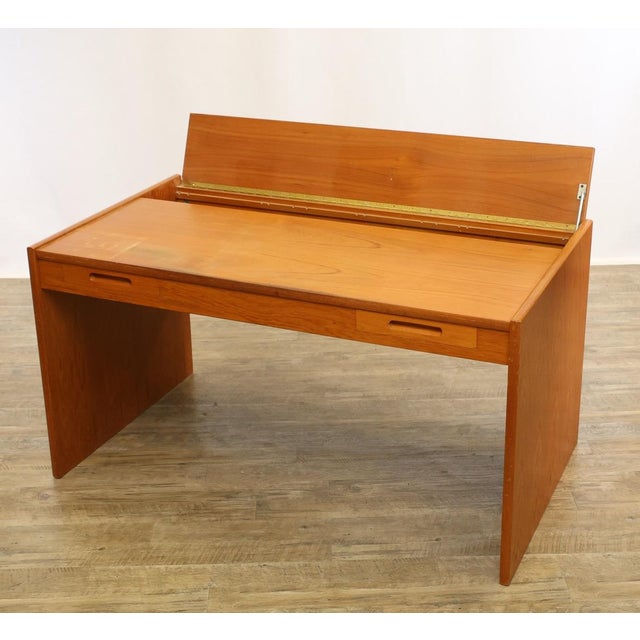 A refined mid-century modern writing desk featuring richly figured teak veneer, clean architectural lines, and a...