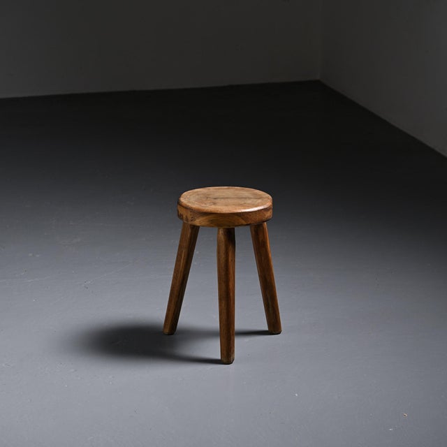 A tripod stool crafted from solid wood in the French Alps around the 1950s. Its thick, circular seat rests on three...
