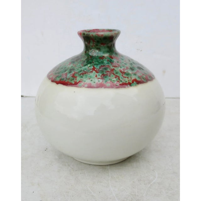 Globular form with creamy white body glaze. The mouth and shoulders are covered in two color glazes mixing and flowing...