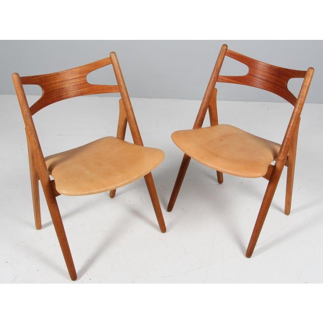 Hans J. Wegner sawbuk dining chairs in oak frame and teak back. Seat upholstered with patinated full grain nature aniline...