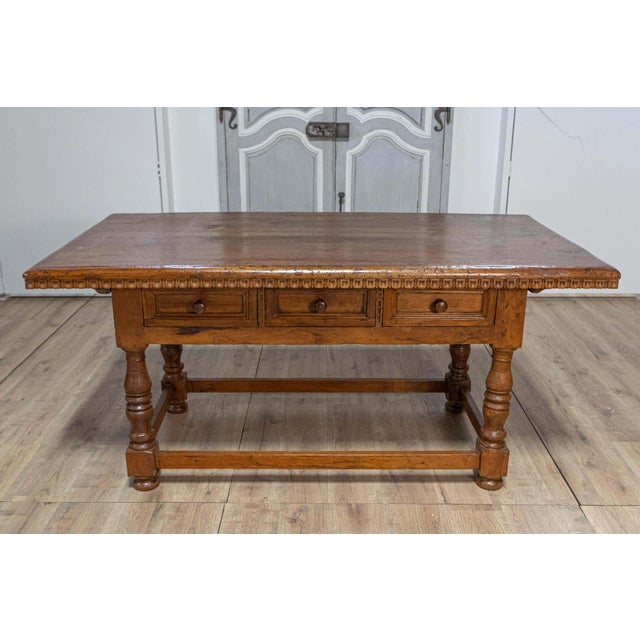 An Italian Tuscan walnut refectory table from circa 1790 with carved scoop motifs, three drawers, turned legs and plain...
