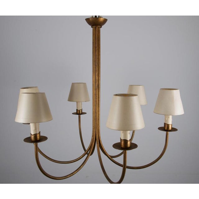 Large brass chandelier from germany, 1970s, designed with six elegantly curved arms rising from a tall central stem. The...