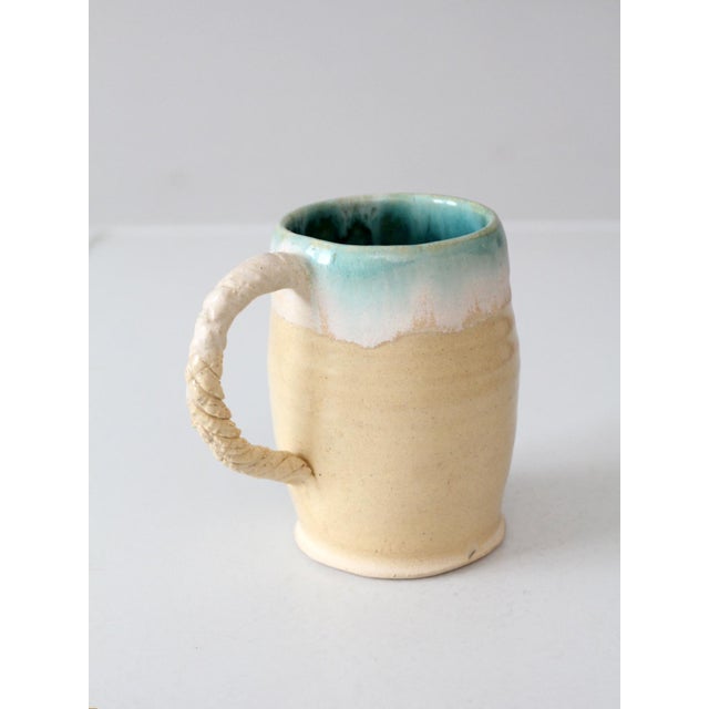 This vintage handmade ceramic mug features a cream glaze that transitions to turquoise green along the rim and interior,...