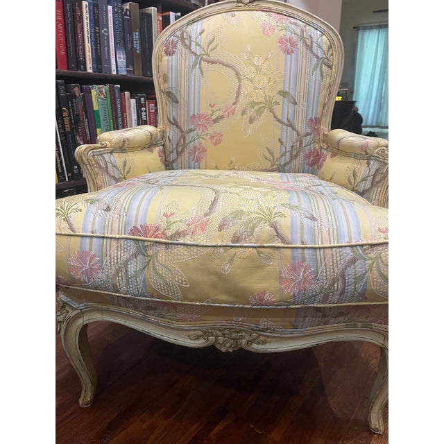 This antique Louis XIV-XV bergere chair is upholstered in a floral print with finely hand carved, painted and distressed...
