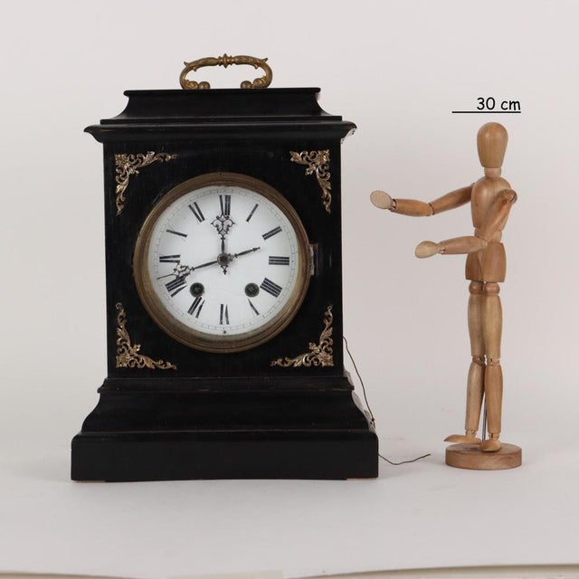Wooden countertop clock with dark patina. Enamelled metal dial with Roman numeral hours protected by a glass cover....