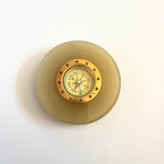 A circular vintage compass paperweight. Features a central compass with brass trim, set in a circular piece of onyx. Taupe...