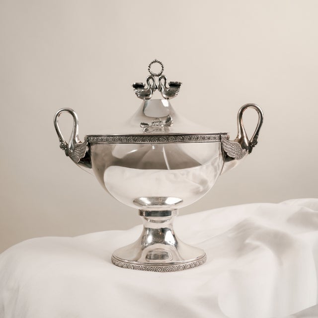 This imposing ornamental tureen embodies the splendor and majesty of the Neoclassical-inspired Empire style. with its cup-...