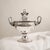 This imposing ornamental tureen embodies the splendor and majesty of the Neoclassical-inspired Empire style. with its cup-...
