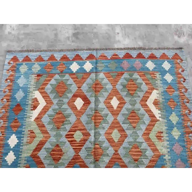 Hand-Woven Afghan Kilim Rug: • Incorporates rich tradition and vibrant colors. • Features geometric design in blue and...