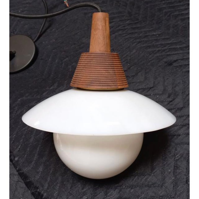Crest Pendant Light by Allied Maker. Features a white canopy with walnut top, milky glass globe, and black base and cord....
