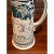 Magnificent vintage German beer stein featuring intricate raised relief scenes and classic green-and-white glazing. This...