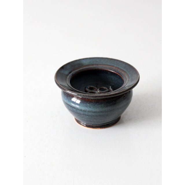 This vintage handmade studio pottery flower frog vase features a rounded bowl, petite foot, and broad flared rim finished...