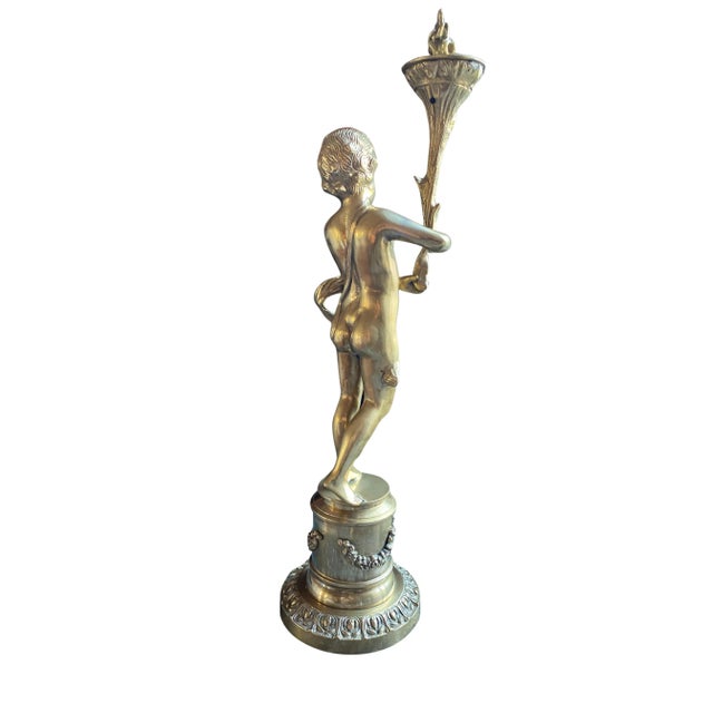 Charming gilded bronze sculpture depicting a young putto (cherub) holding a torch. The child, standing on a pedestal...
